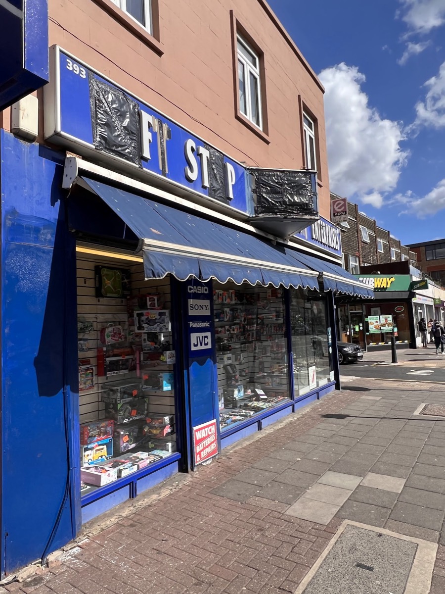 Raj Enterprises' blue shopfront on Bethnal Green Road on a sunny day, next to Subway